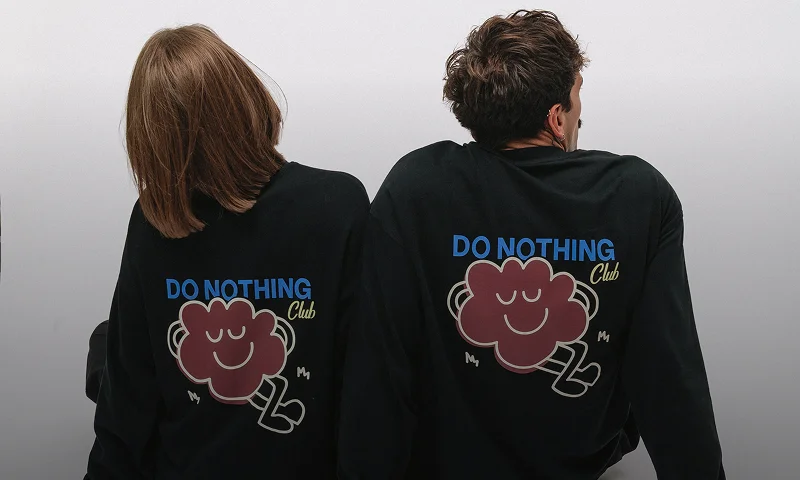 Dwie osoby ujęte od tyłu w czarnych koszulkach z długim rękawem, ozdobionych rysunkiem uśmiechniętej chmurki oraz napisem „Do Nothing Club”. Baner odsyła do kategorii i prezentuje wyraziste longsleeve Kubota stworzone z myślą o miłośnikach swobodnego, miejskiego stylu.